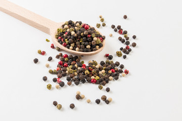colored pepper peppercorns on wooden spoon on white background