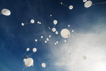 White balloons fly up into the blue sky. The release of festive balloons in the clouds. Celebration and happiness. Air gel balls in the atmosphere.
