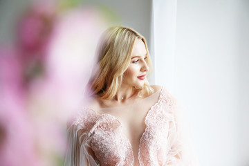 Young beautiful woman with blond wavy hairstyle wearing tender pink wedding dress. Fragile bride portrait in full length maxidress. Close up, copy space, background.