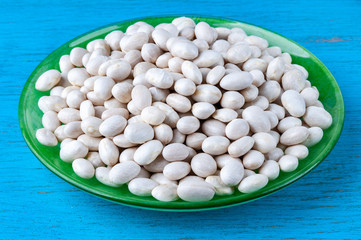 White beans in a green plate on a blue wooden background.