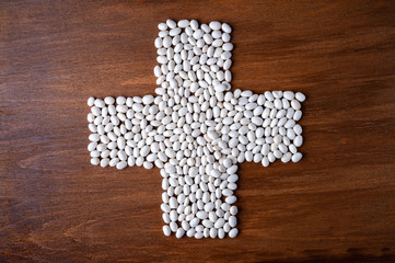 Many white beans poured into the shape of a cross on a wooden background.
