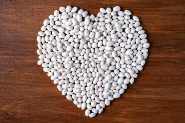 Many white beans poured into the shape of a heart on a wooden background.