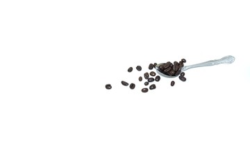 In selective focus many dark roasted coffee beans on a stainless spoon and on a floor, White isolated background 