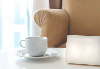 White sign cardboard with copy space next to the tea cup on a white table. Hotel or bussiness interior