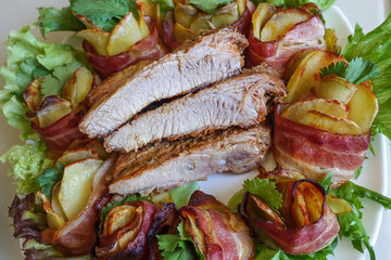 Grilled pork ribs on a white plate with greens, lettuce and meat rolls