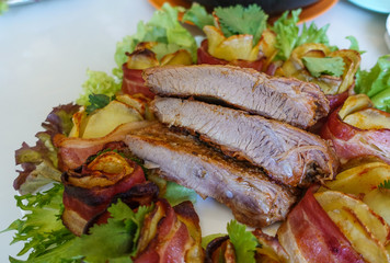 Grilled pork ribs on a white plate with greens, lettuce and meat rolls