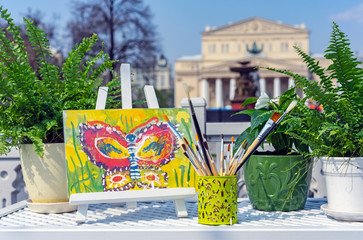 Watercolor brushes and easel on the background of the Bolshoi Theater in Moscow.