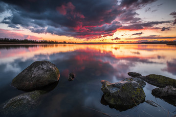 Feuriger Sonnenuntergang über dem Sehlendorfer Binnensee mit Steinen im Vordergrund und...