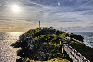 The south stack lighthouse in North Wales with a thrilling sky and the soon setting sun in the background.