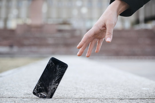 Close up of young woman reaches out to her broken smartphone with cracked screen glass