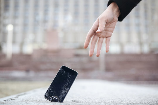 Close up of young woman pick up her broken smartphone with cracked screen glass