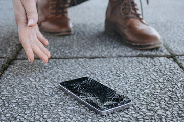Young woman picks up her broken smartphone with cracked screen after falling