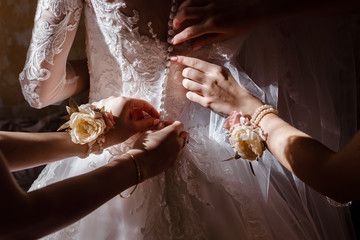Bridesmaid helping bride fasten corset and getting her dress, preparing bride in morning for the...