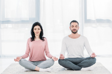 woman and man with eyes closed sitting in Lotus Pose and meditating at home