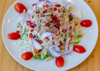 Spicy tuna salad In a white plate, salad this dish consist of tuna, lettuce, chinese cabbage, carrot onion red chilli rough cut, dressing and tomato half cut Used to arrange dishes.