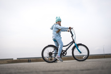 A girl in a hat and a blue sweater on a bicycle stopped and looks around.