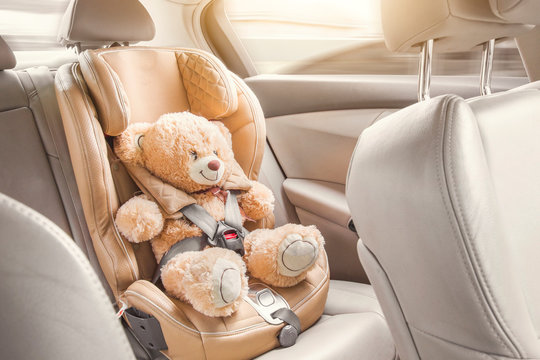 Baby child seat car. A beige teddy bear is fastened with seat belts in a car seat. Travel by car