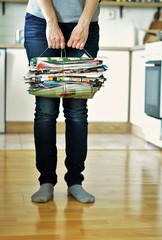elderly woman holding old magazines for recycling at home