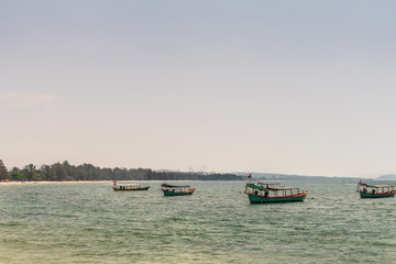 Obraz premium Sihanoukville, Cambodia - March 15, 2019: Closeup of Small wooden fishing boats off Ochheuteal Beach. Horizon formed by Jungle vegetation on shore.