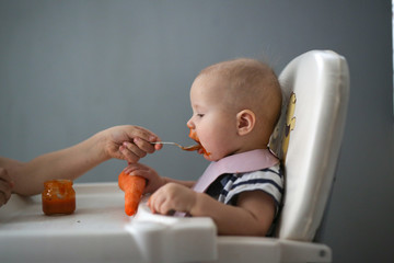 Older sister feeds baby puree, fresh baby carrots