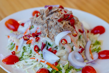 Spicy tuna salad In a white plate, salad this dish consist of tuna, lettuce, chinese cabbage, carrot onion red chilli rough cut, dressing and tomato half cut Used to arrange dishes.