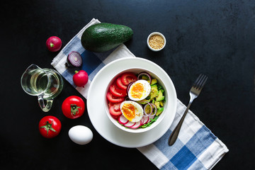 healthy bowl with boiling egg fresh tomatoes avocado radish arugula red onion sesame seeds fork napkin and ingredients  on black background top view 