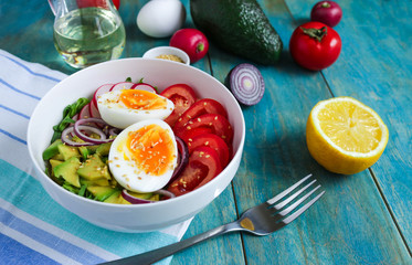 healthy bowl with boiling egg halves tomatoes avocado red onion radish arugula sesame seeds  lemon and other ingredients on blue wooden table close up