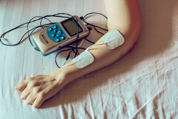 Small grey electro stimulator and white electrodes on a laying woman’s hand – Electric device...
