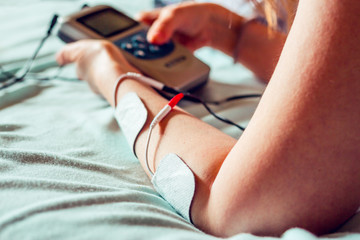 Woman laying down using a small sized electro stimulator for home use – Electric device that helps in pain relief and massage - Medical equipment for alternative therapies