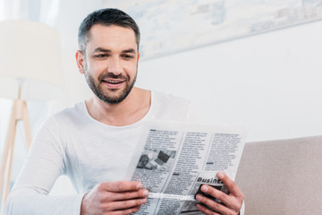 Fototapeta na wymiar handsome smiling bearded man reading newspaper at home