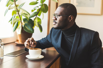 Young handsome dark-skinned businessman drinks coffee in a cafe.