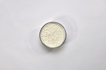 White wheat flour in a round cup on a light background. Top view, in the center.