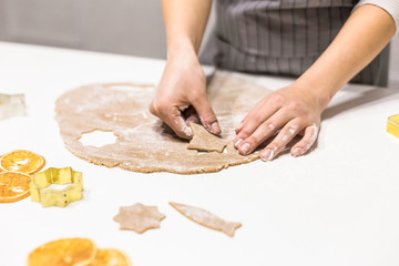Young pretty woman prepares the dough and bakes gingerbread and cookies in the kitchen. She makes a star shape on the dough. Merry Christmas and Happy New Year.