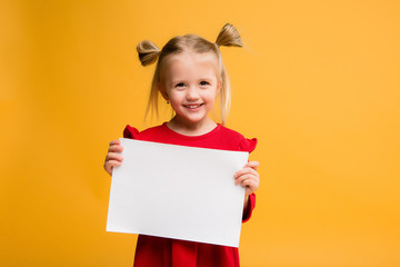 baby girl holding white sheet.Cute little girl with white sheet of paper.yellow background.copy...