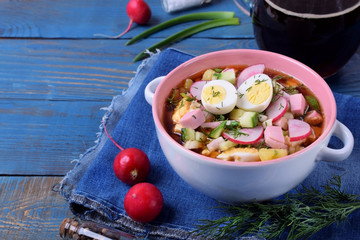 Russian cold soup Okroshka with vegetables, sausage, eggs and kvass in a ceramic bowl on the blue table