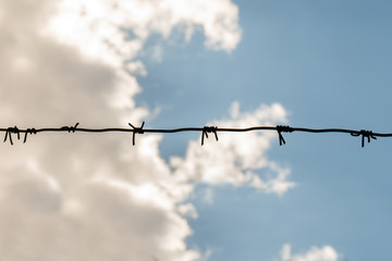 Barbed wire fence detail, gray clouds with blue sky in the background. deprivation of liberty...
