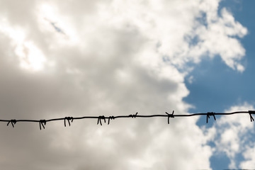 barbed wire against cloudy sky. Imprisonment concept. wire with clusters of short, sharp spikes set...