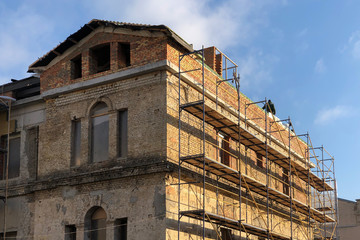 the facade of the old building in scaffolding against blue sky in daytime. exterior of old brick building Under Renovation.