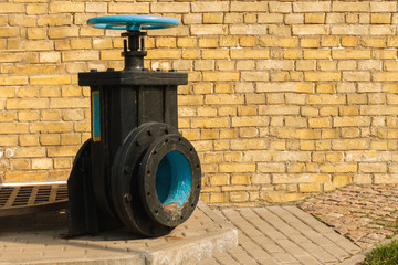 old blue valve on the black basement with brick wall in the background. control consisting of a mechanical device for controlling the flow of a fluid.