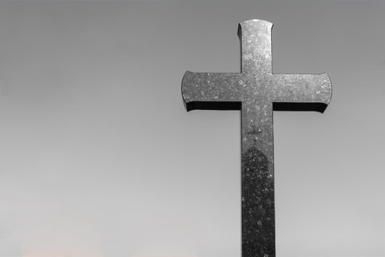 stone cross in a graveyard with copy space for text. crucifix against a gray background.
