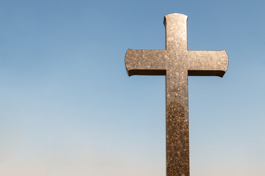 sunlight on granite cross against the blue sky, copy space for text. concept of Christianity. Granite cross on the sky background.