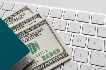 fan of hundred dollar bills in a green passport that lies on the white keyboard. passport, dollars bills and computer keyboard as a concept of online ticket booking.
