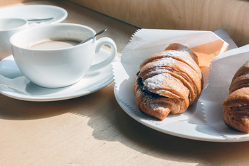 fresh baked croissants and white Coffee cup on wooden background, instagram filter. mug of coffee, croissants with icing sugar wrapped in paper, selective focus