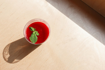Portion of coconut panna cotta with raspberry jam and mint leaf in a plastic cup on a wooden...