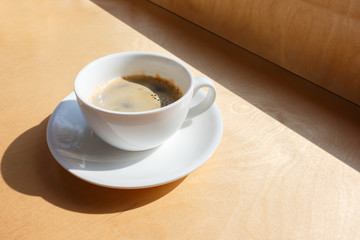 white cup of coffee on a saucer against the background of wooden window sill, Coffee morning ritual.