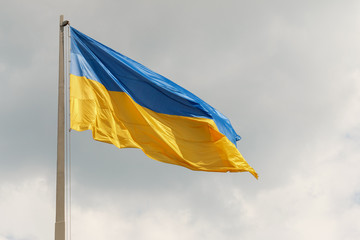 Blue and yellow Ukrainian national flag on a flagpole against a gray sky and sun, view from below. The symbol of 2019 ballot and poll in Ukraine.