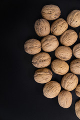 Walnuts in the shell lying on black surface, top view. Background of round walnuts. Healthy nuts and seeds composition.