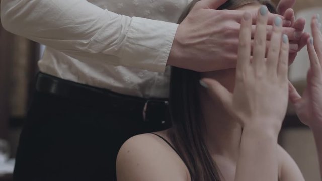 Unrecognizable man in white shirt covering eyes oy pretty young woman sitting in the restaurant. The cute couple has a date. Concept of love, relationship, closeness