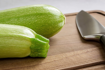 Two fresh green zucchini and professional chef knife on a brown wooden cutting board. Cook at home. Fresh vegetables, and healthy vegetarian food.