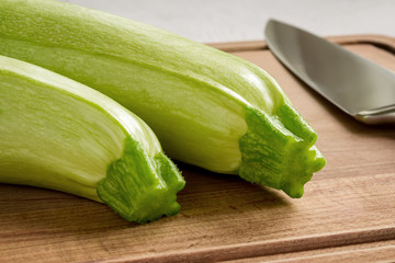 Two fresh green courgettes and professional chef knife on a brown wooden cutting board. Cook at home. Fresh vegetables and healthy vegetarian food.